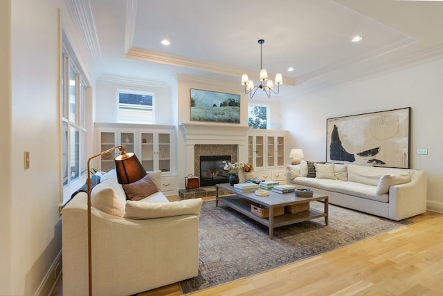 living room with an inviting chandelier, wood-type flooring, a raised ceiling, and crown molding