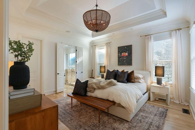 bedroom with ensuite bathroom, light hardwood / wood-style flooring, a tray ceiling, and multiple windows