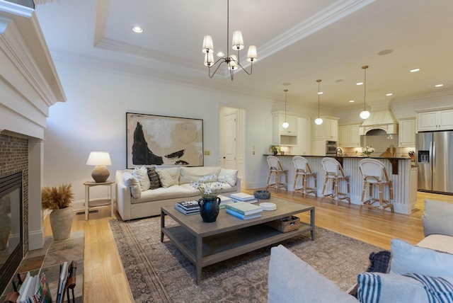 living room featuring a brick fireplace, a chandelier, crown molding, and wood-type flooring