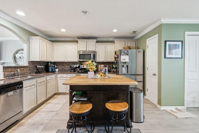 kitchen with stainless steel appliances, dark stone counters, sink, backsplash, and ornamental molding