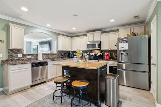 kitchen with a center island, appliances with stainless steel finishes, sink, ornamental molding, and a breakfast bar area