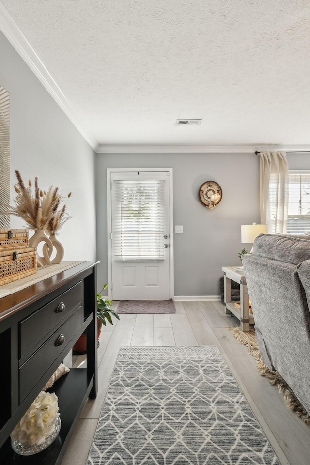 foyer entrance featuring light hardwood / wood-style floors, a textured ceiling, ornamental molding, and a healthy amount of sunlight