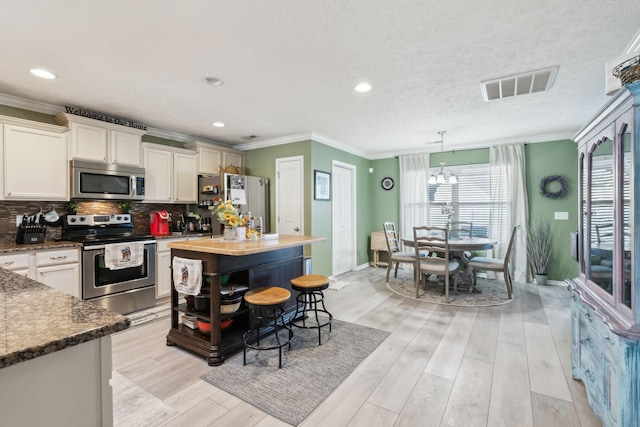 kitchen with appliances with stainless steel finishes, a kitchen island, ornamental molding, an inviting chandelier, and pendant lighting