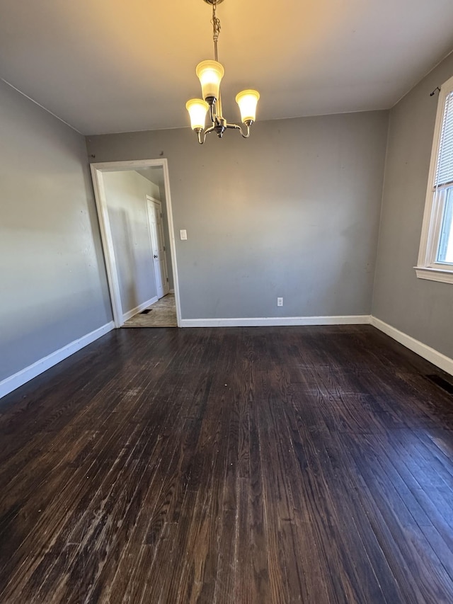 spare room featuring an inviting chandelier and dark hardwood / wood-style floors