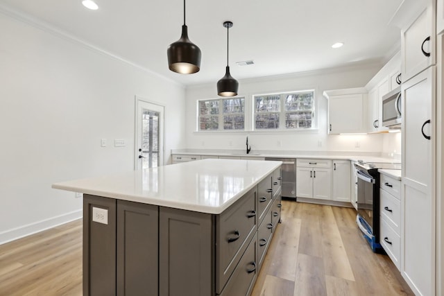 kitchen featuring appliances with stainless steel finishes, white cabinetry, hanging light fixtures, a center island, and light hardwood / wood-style floors