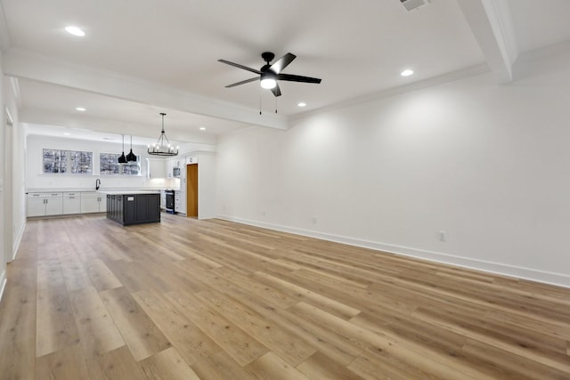 unfurnished living room with sink, crown molding, light hardwood / wood-style floors, ceiling fan with notable chandelier, and beamed ceiling