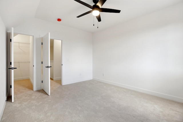 unfurnished bedroom with a spacious closet, vaulted ceiling, light carpet, a closet, and ceiling fan