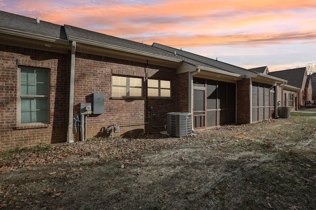 property exterior at dusk with central AC unit and a lawn