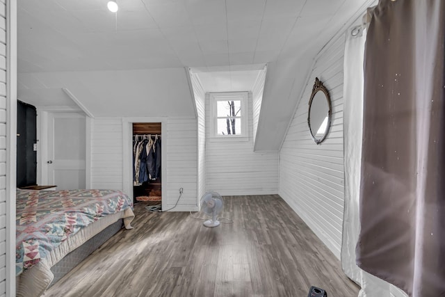 unfurnished bedroom with a spacious closet, hardwood / wood-style flooring, a closet, and wood walls