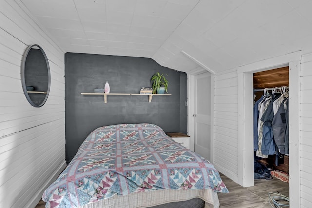 bedroom featuring a walk in closet, wooden walls, a closet, vaulted ceiling, and hardwood / wood-style flooring