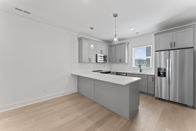 kitchen with stainless steel appliances, pendant lighting, kitchen peninsula, and gray cabinets