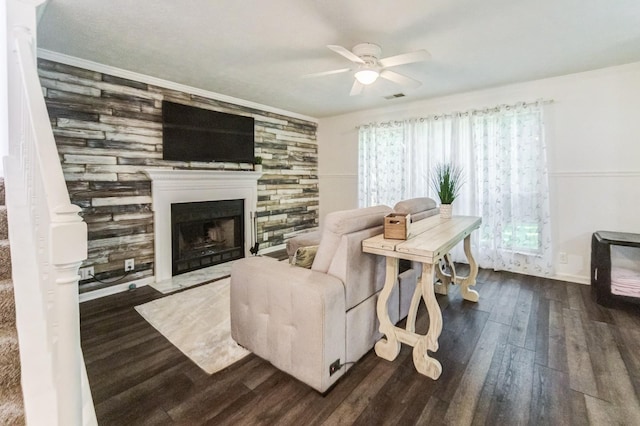 living room featuring ceiling fan, ornamental molding, a large fireplace, and dark hardwood / wood-style flooring