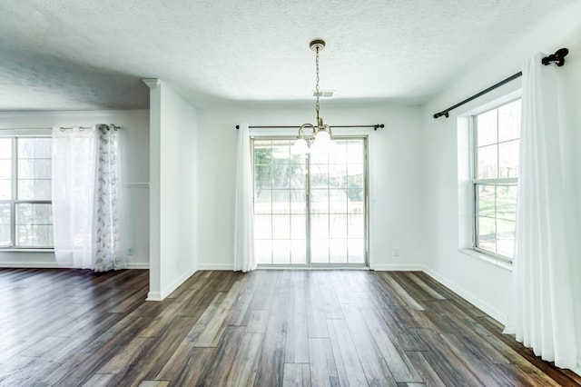 unfurnished dining area featuring a wealth of natural light, a textured ceiling, and dark hardwood / wood-style flooring