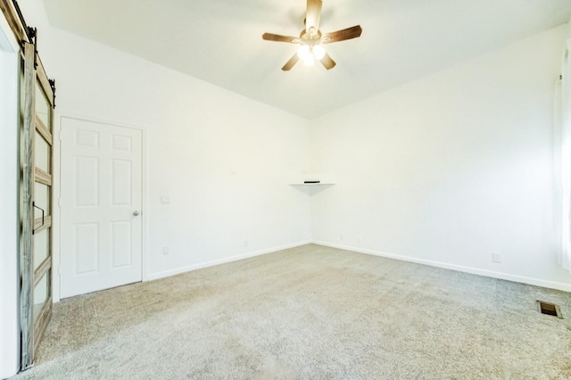 carpeted empty room featuring a barn door and ceiling fan