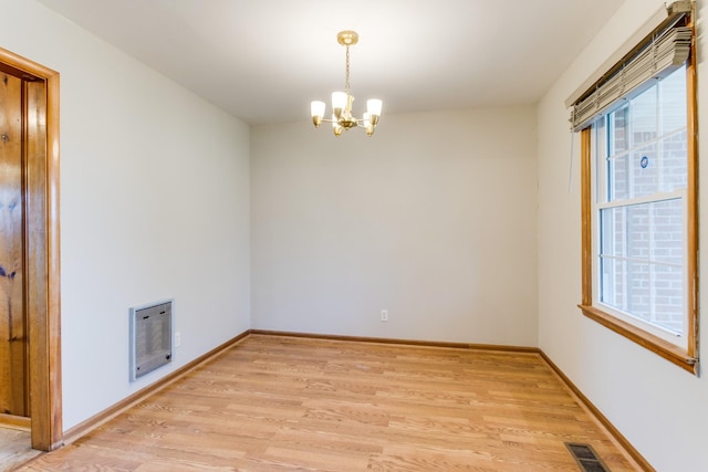 empty room with heating unit, a chandelier, and light hardwood / wood-style flooring