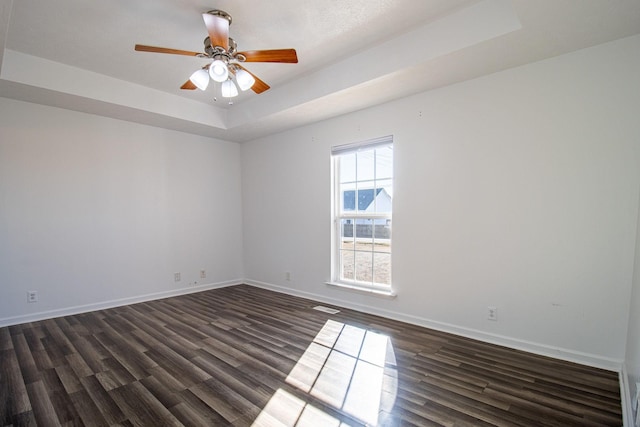 unfurnished room with dark wood-type flooring, a raised ceiling, and ceiling fan