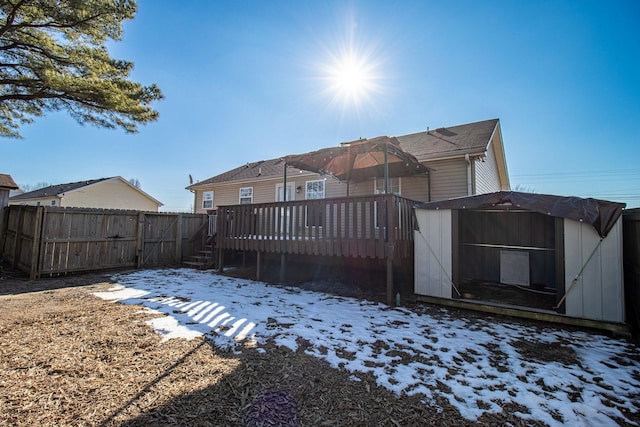 snow covered house with a wooden deck and a storage unit