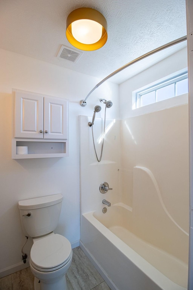 bathroom featuring toilet, shower / bath combination, and a textured ceiling