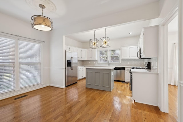 kitchen with stainless steel appliances, white cabinetry, hanging light fixtures, and a center island