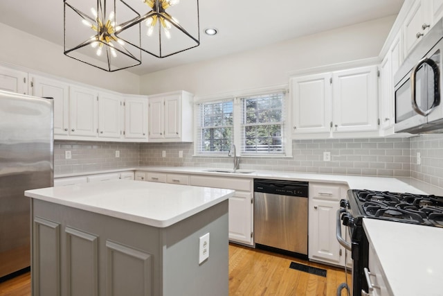 kitchen with appliances with stainless steel finishes, a kitchen island, pendant lighting, white cabinets, and sink