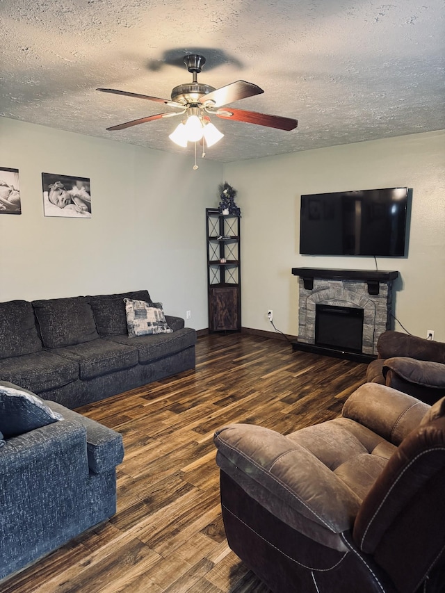 living room with ceiling fan, a textured ceiling, dark hardwood / wood-style floors, and a stone fireplace