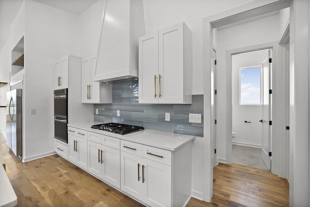 kitchen with stainless steel appliances, custom exhaust hood, light hardwood / wood-style flooring, and white cabinets