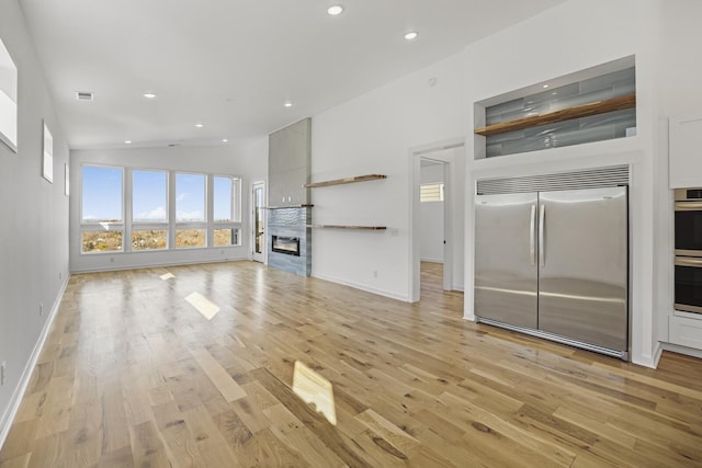 unfurnished living room featuring lofted ceiling, a premium fireplace, and light hardwood / wood-style flooring