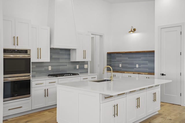 kitchen with white cabinetry, an island with sink, stainless steel appliances, decorative backsplash, and sink