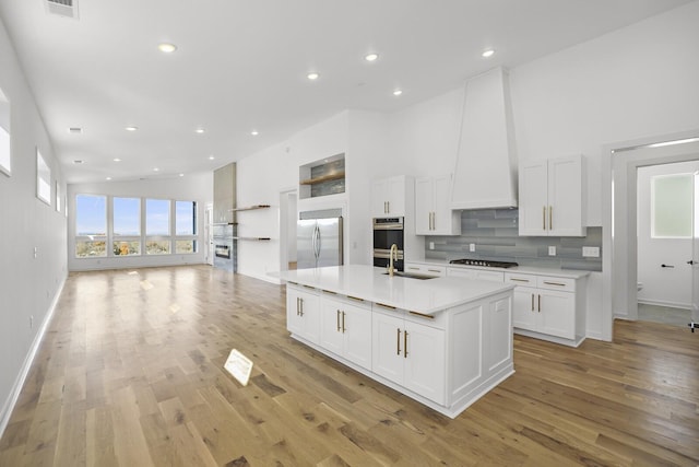 kitchen with white cabinetry, stainless steel appliances, light hardwood / wood-style floors, sink, and a center island with sink