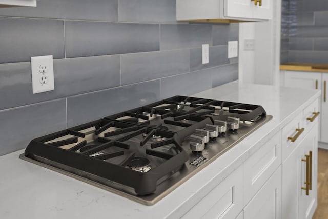 interior details featuring tasteful backsplash, stainless steel gas cooktop, and white cabinetry