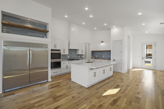 kitchen featuring white cabinetry, stainless steel appliances, tasteful backsplash, an island with sink, and sink