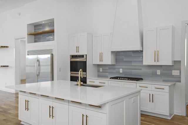 kitchen with stainless steel appliances, light hardwood / wood-style floors, white cabinetry, and a kitchen island with sink