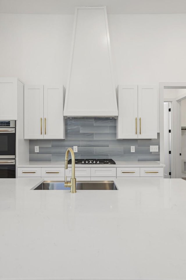 kitchen featuring stainless steel appliances, sink, white cabinets, and custom range hood