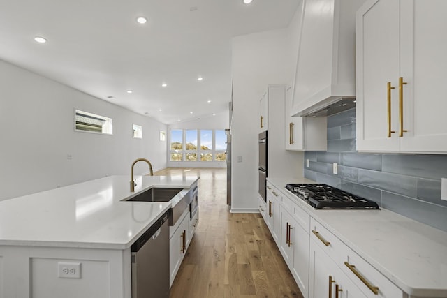 kitchen with appliances with stainless steel finishes, white cabinetry, an island with sink, decorative backsplash, and custom range hood