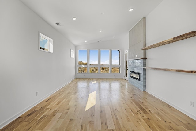 unfurnished living room featuring a tiled fireplace, vaulted ceiling, and light hardwood / wood-style flooring