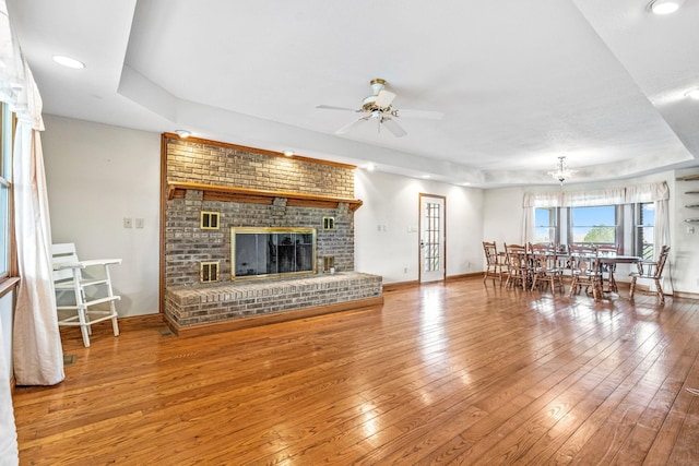 unfurnished living room with a tray ceiling, a fireplace, ceiling fan with notable chandelier, and hardwood / wood-style flooring