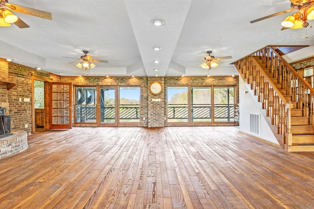 unfurnished living room featuring a textured ceiling, brick wall, a wood stove, and wood-type flooring