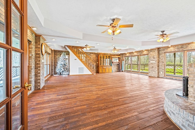 unfurnished living room with ceiling fan, brick wall, a textured ceiling, and hardwood / wood-style floors