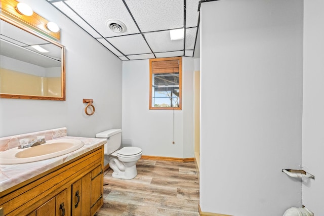 bathroom featuring wood-type flooring, a drop ceiling, toilet, and vanity