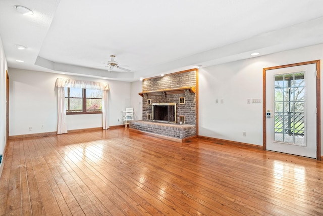 unfurnished living room with ceiling fan, a raised ceiling, a fireplace, and light hardwood / wood-style flooring