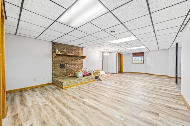 basement featuring a brick fireplace, a drop ceiling, and light wood-type flooring