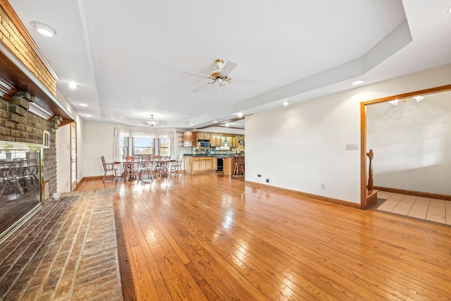 unfurnished living room featuring a raised ceiling, ceiling fan, a fireplace, and hardwood / wood-style floors