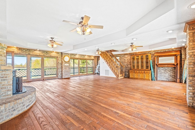 unfurnished living room featuring a wood stove, brick wall, a textured ceiling, and hardwood / wood-style floors