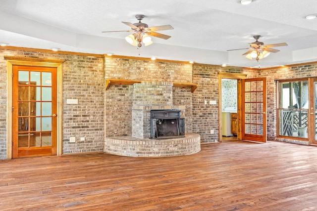 unfurnished living room with ceiling fan, a wood stove, wood-type flooring, french doors, and a textured ceiling