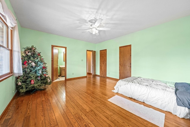 bedroom featuring ceiling fan, ensuite bath, multiple windows, and light hardwood / wood-style flooring