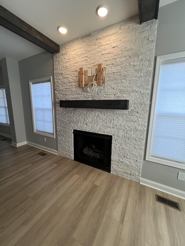 unfurnished living room with beam ceiling, a fireplace, a wealth of natural light, and hardwood / wood-style floors