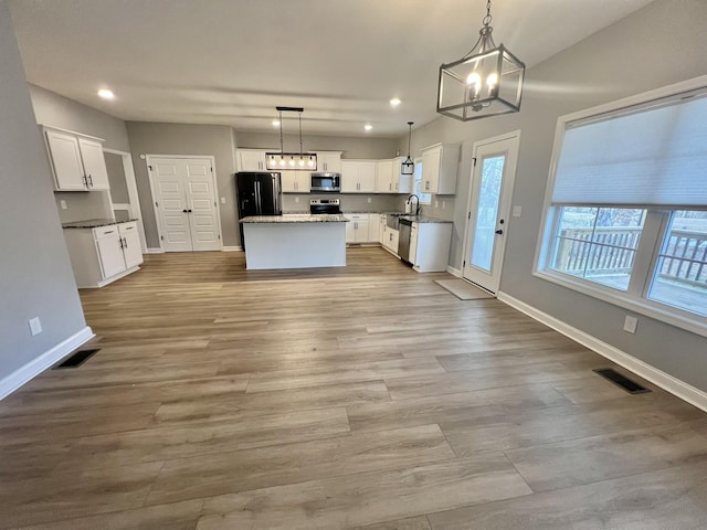 kitchen featuring white cabinets, a center island, appliances with stainless steel finishes, decorative light fixtures, and light hardwood / wood-style flooring