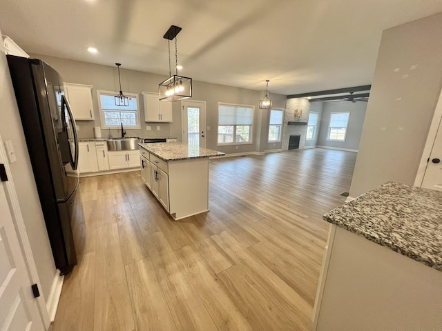 kitchen featuring white cabinets, a kitchen island, open floor plan, freestanding refrigerator, and a sink