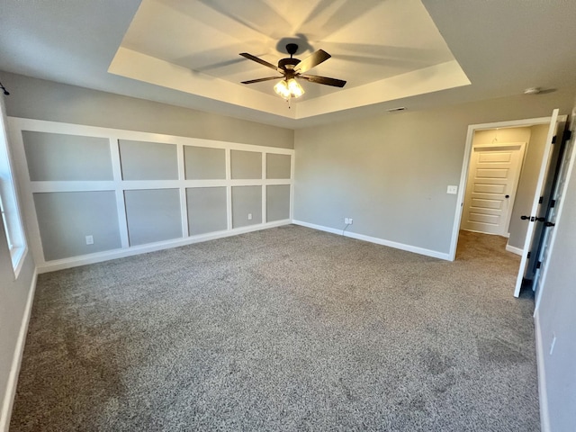 unfurnished bedroom featuring carpet floors, baseboards, a tray ceiling, and a ceiling fan