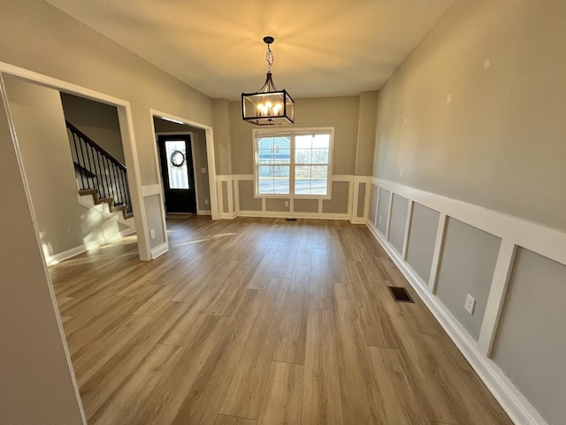 interior space featuring a notable chandelier, visible vents, a decorative wall, wood finished floors, and stairs